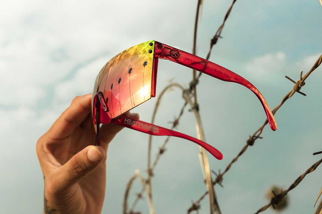 Hand holding up the Heat Wave Visual Lazer Face Sunglasses with neon red frame and atmosphere blue red lens.