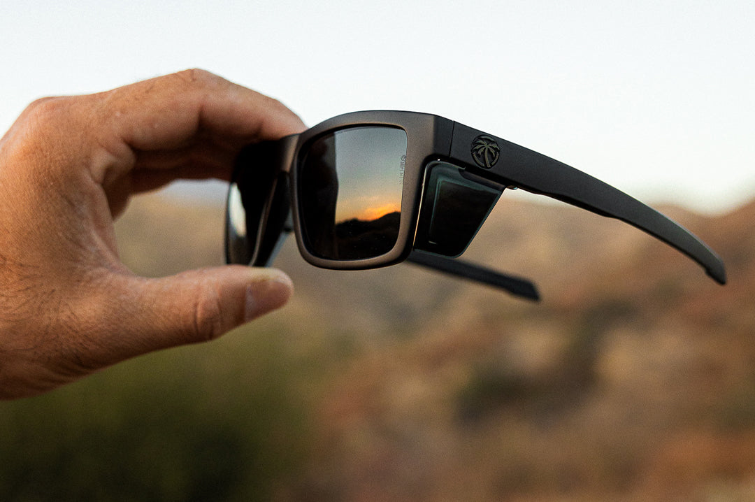 Hand holding the Heat Wave Visual Performance Lazer Face Sunglasses with black frame and ultra black lenses.