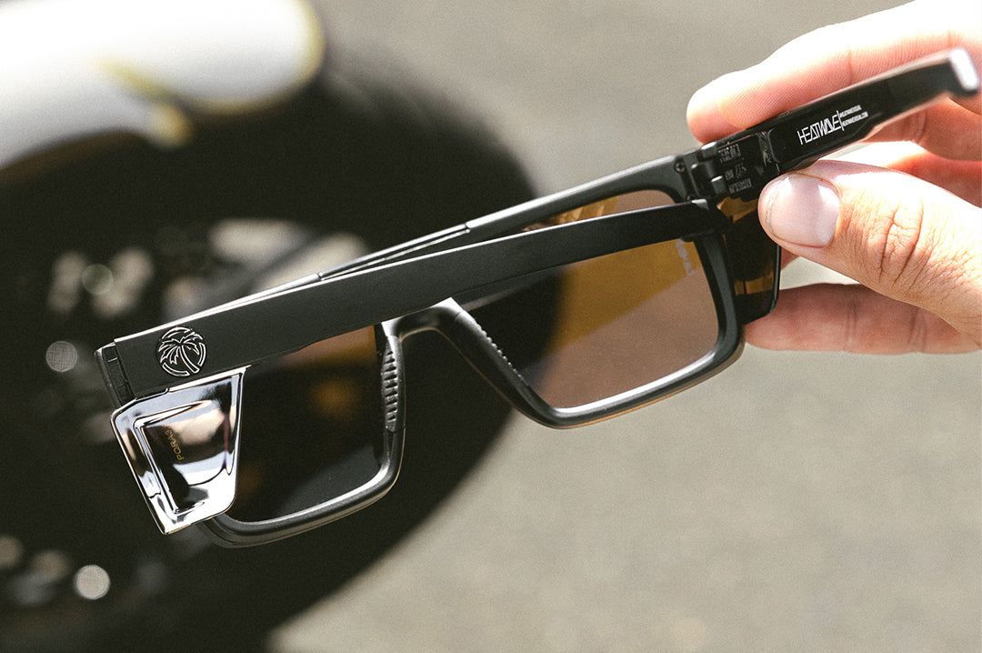 Hand holding the Heat Wave Visual Performance Quatro Sunglasses with black frame, silver lens and matching colored side shields. 