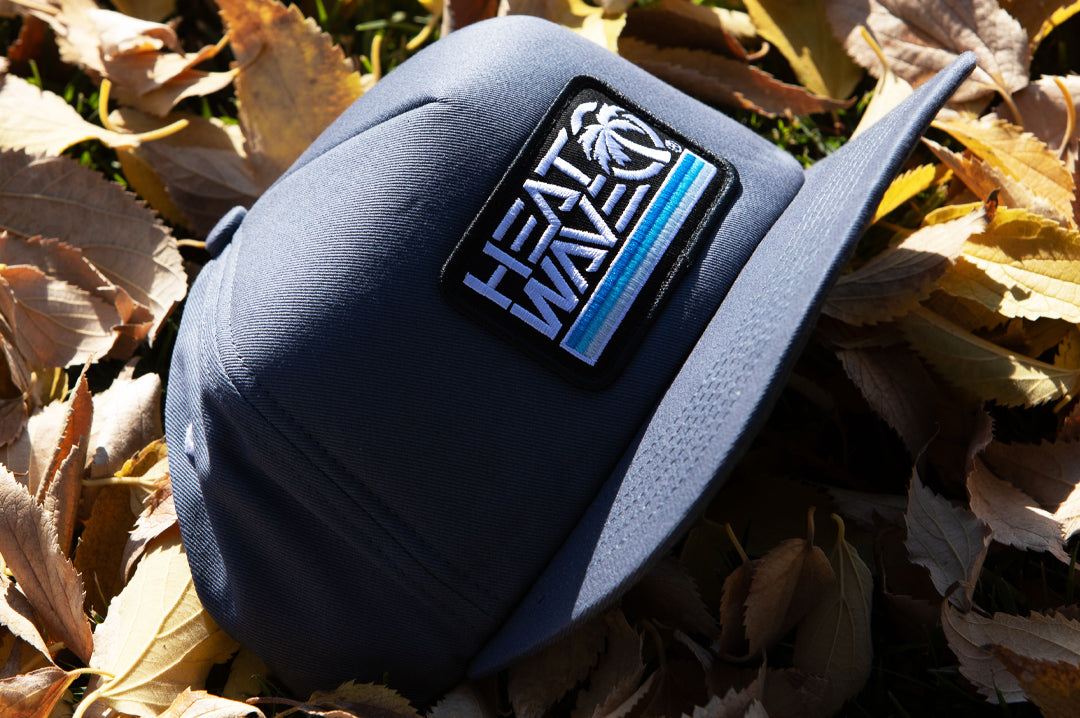 The Heat Wave Visual Retro Stripe Slate Hat lying on top of some leaves. 