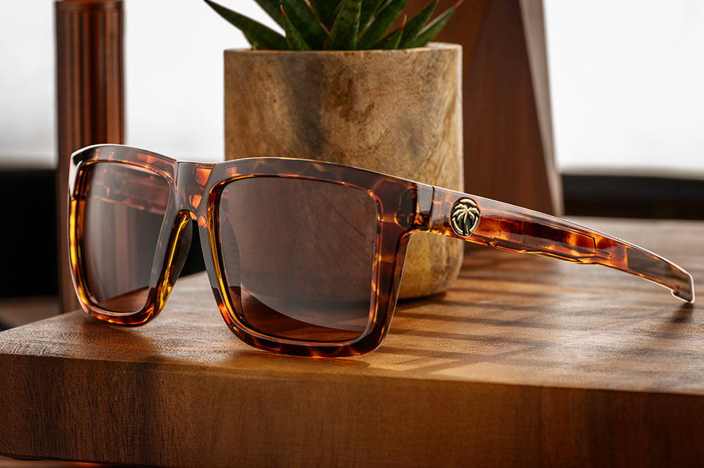Heat Wave Visual Performance XL Vise Tortoise Sunglasses on a wooden surface with a plant in the background.