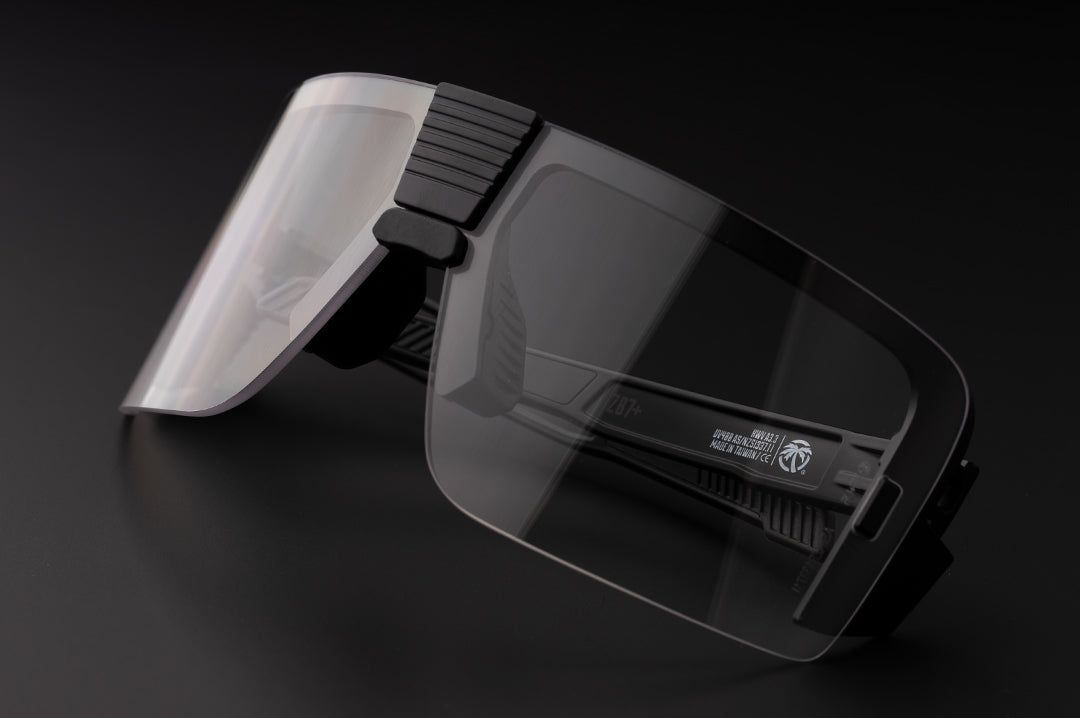 Lying on a table is the Heat Wave Visual XL Vector Sunglasses with black frame and clear lens.