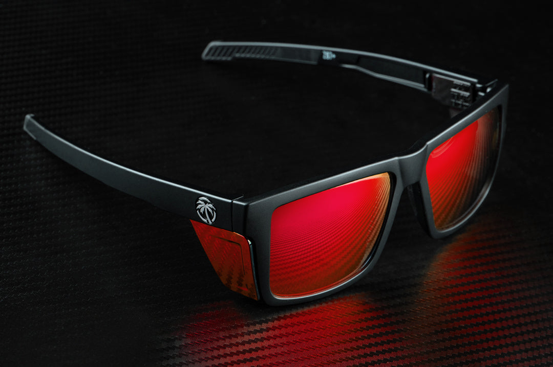 Sitting on a table is the Heat Wave Visual Performance Vise Sunglasses with black frame, firestorm red lenses and matching colored side shields.