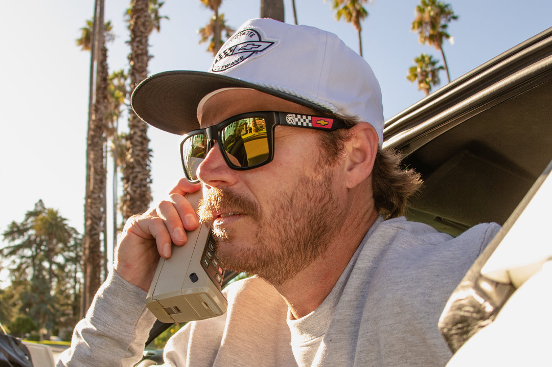 Justin on a phone call wearing the Heat Wave Visual Vise Sunglasses with black frame, corvette print arms and gold lenses.
