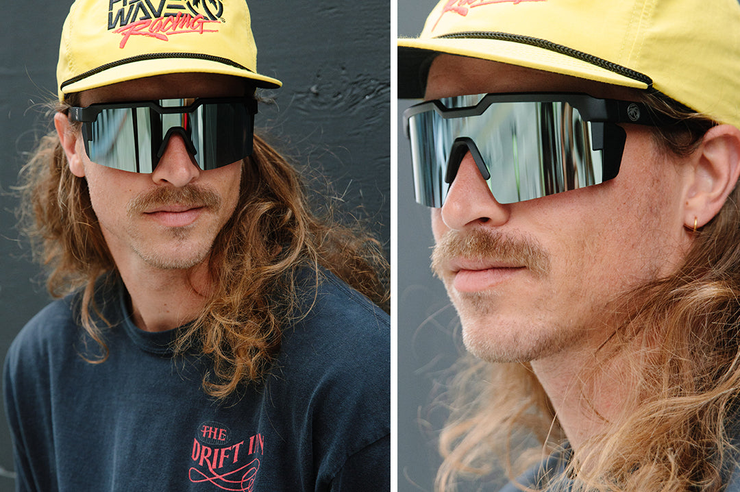 Long haird mustached man wearing Heat Wave Visual Future Tech Sunglasses with black frame and arctic chrome light blue lens.