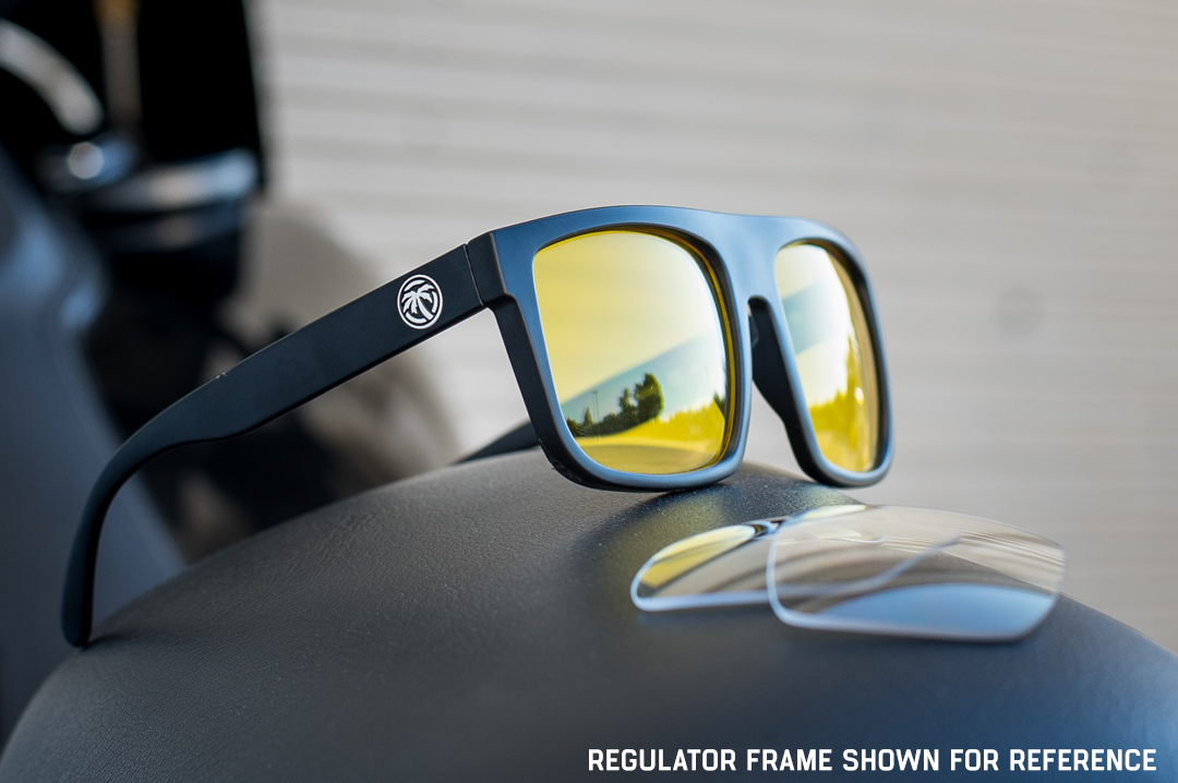 Sitting on motorcyle seat is the Heat Wave Visual Regulator Sunglasses with black frame and hi vis lenses and extra clear lenses.