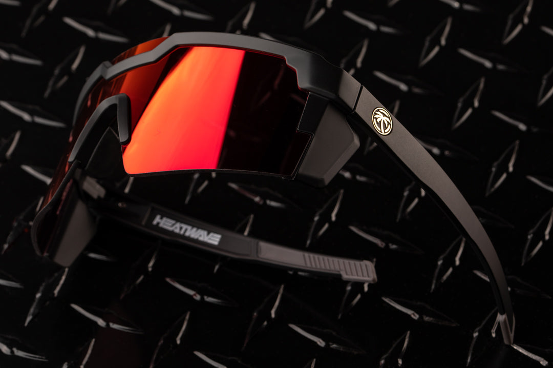 Side view of the Heat Wave Visual Future Tech Sunglasses with black frame and firestorm red lens on a black table. 