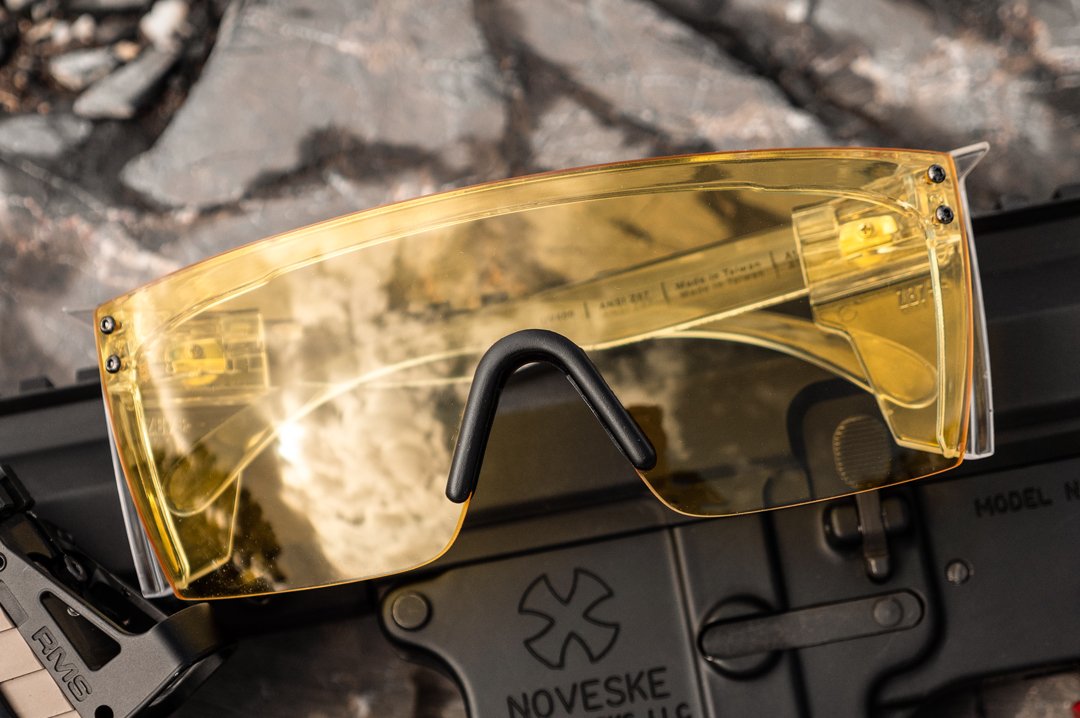 Heat Wave Visual Lazer Face Z87 Sunglasses with clear frame, black nose piece and hi-vis yellow lens outside on a gun. 