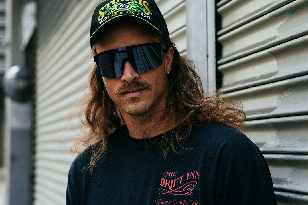 Long haired mustached man wearing Heat Wave Visual Future Tech Sunglasses with black frame and silver lens.