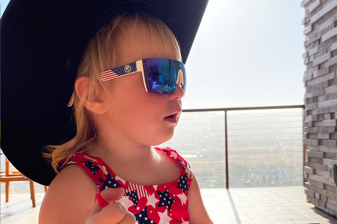 Toddler girl wearing Heat Wave Visual Lazer Face kids sunglasses white frame, USA print arms and galaxy blue lens.