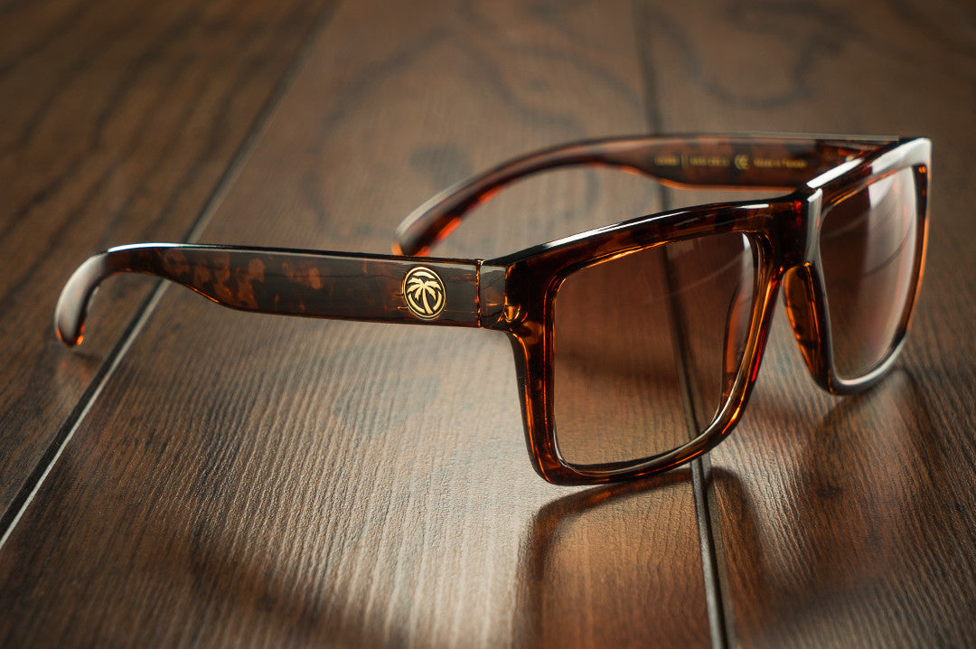 Side view of Heat Wave Visual Vise Sunglasses with tortoise frame and brown gradient lenses on a wood floor. 