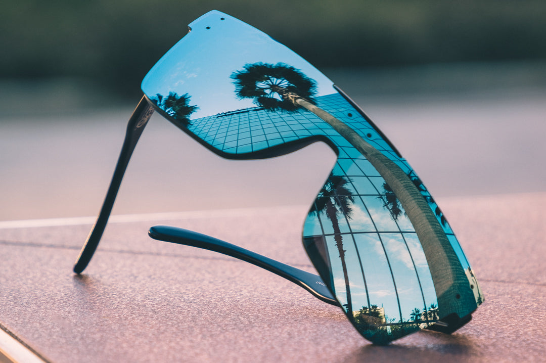 Heat Wave Visual Quatro Sunglasses with black frame and arctic chrome lens lying on concrete reflecting a building.