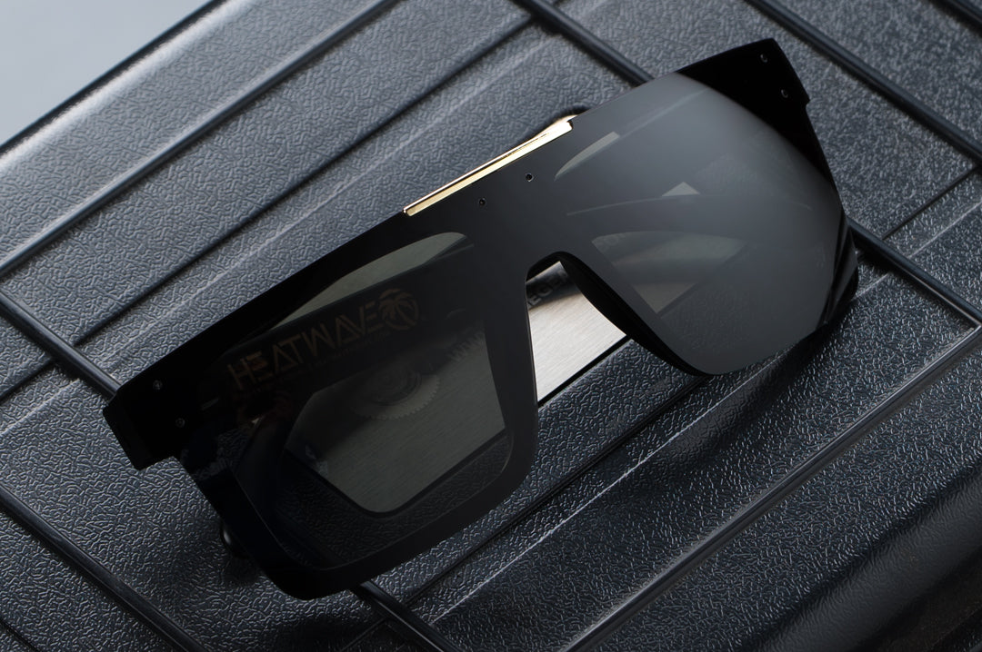 Heat Wave Visual Quatro Sunglasses with black frame, gold bar and black lens on a pelican case.