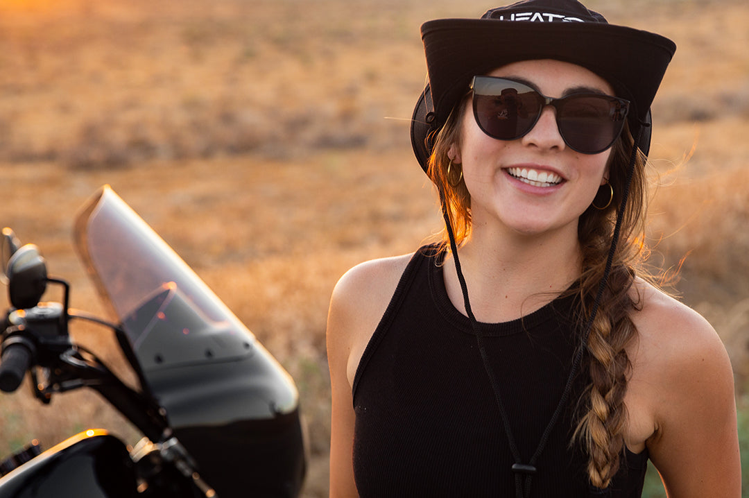 Young woman motorcyclist wearing Heat Wave Visual Womens Carat Sunglasses with black frame and black lenses.