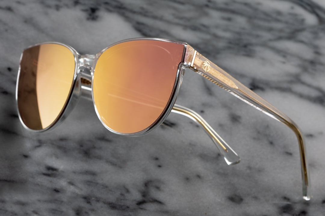 Close up of Heat Wave Visual Womens Carat Sunglasses with clear sparkle frame and rose gold lenses.