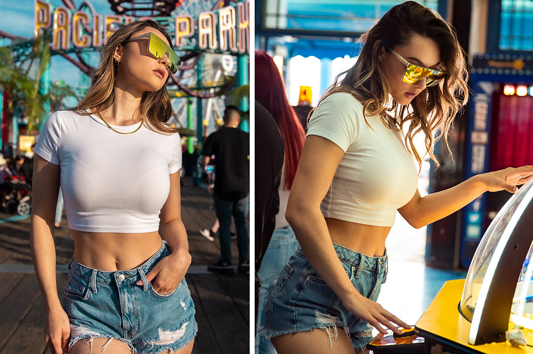 Young woman at arcade wearing Heat Wave Visual Womens Clarity Sunglasses with marble frame and gold lens.