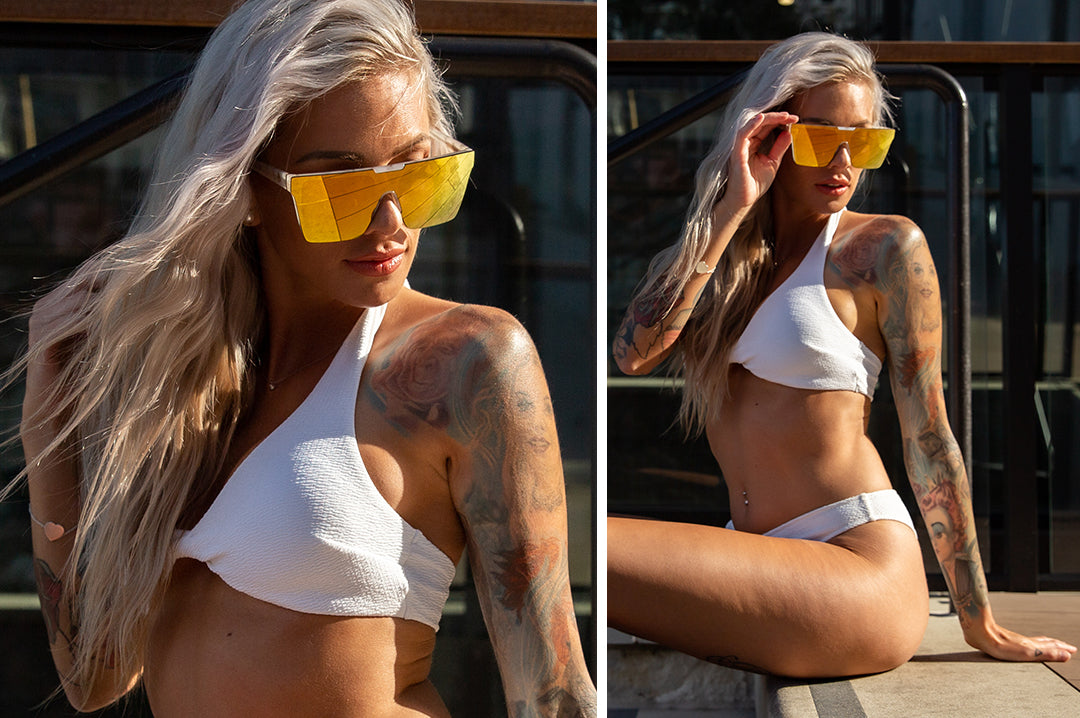 Woman in swimsuit wearing Heat Wave Visual Womens Clarity Sunglasses with marble frame and gold lens.