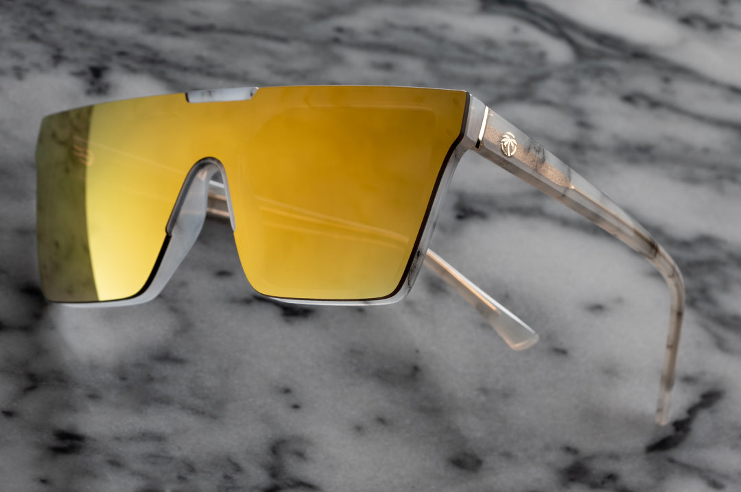 Heat Wave Visual Womens Clarity Sunglasses with marble frame and gold lens against marble background.