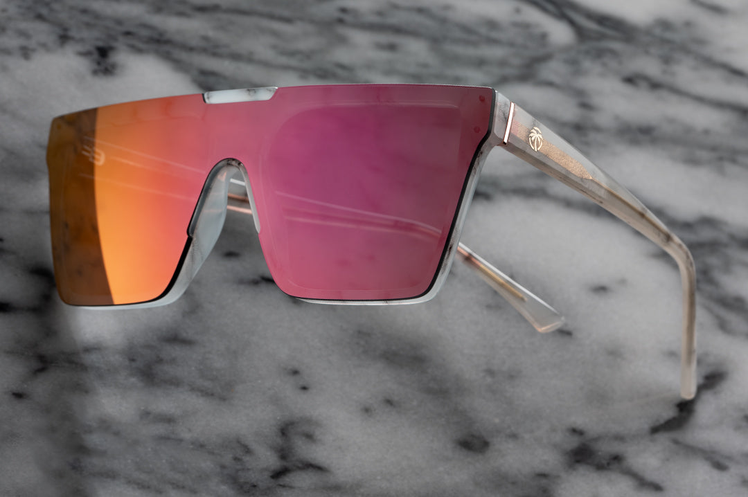 Heat Wave Visual Womens Clarity Sunglasses with marble frame and fuchsia lens against marble background.