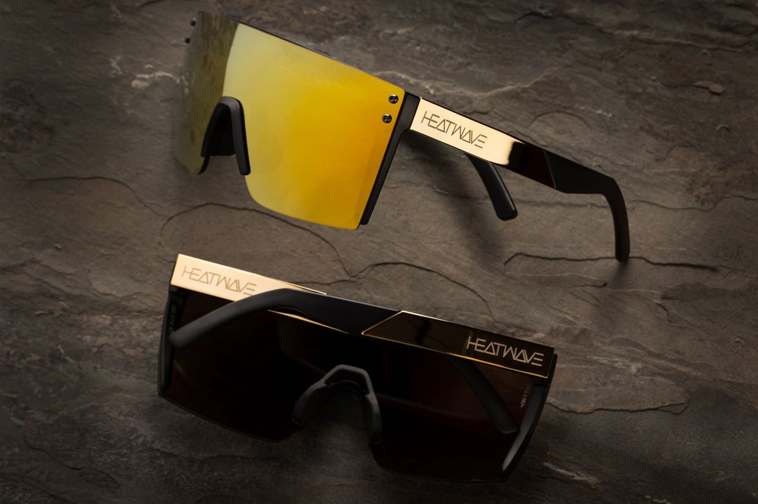 Two Heat Wave Visual Lazer Face Sunglasses with black frame, gold metal arms and gold lens on a slab of rock. 