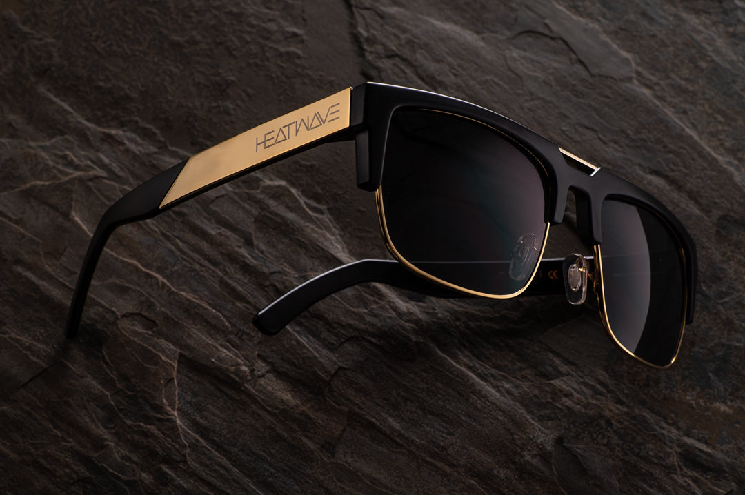 Heat Wave Visual Interceptor Sunglasses with black gold frame and black lenses lying on granite.