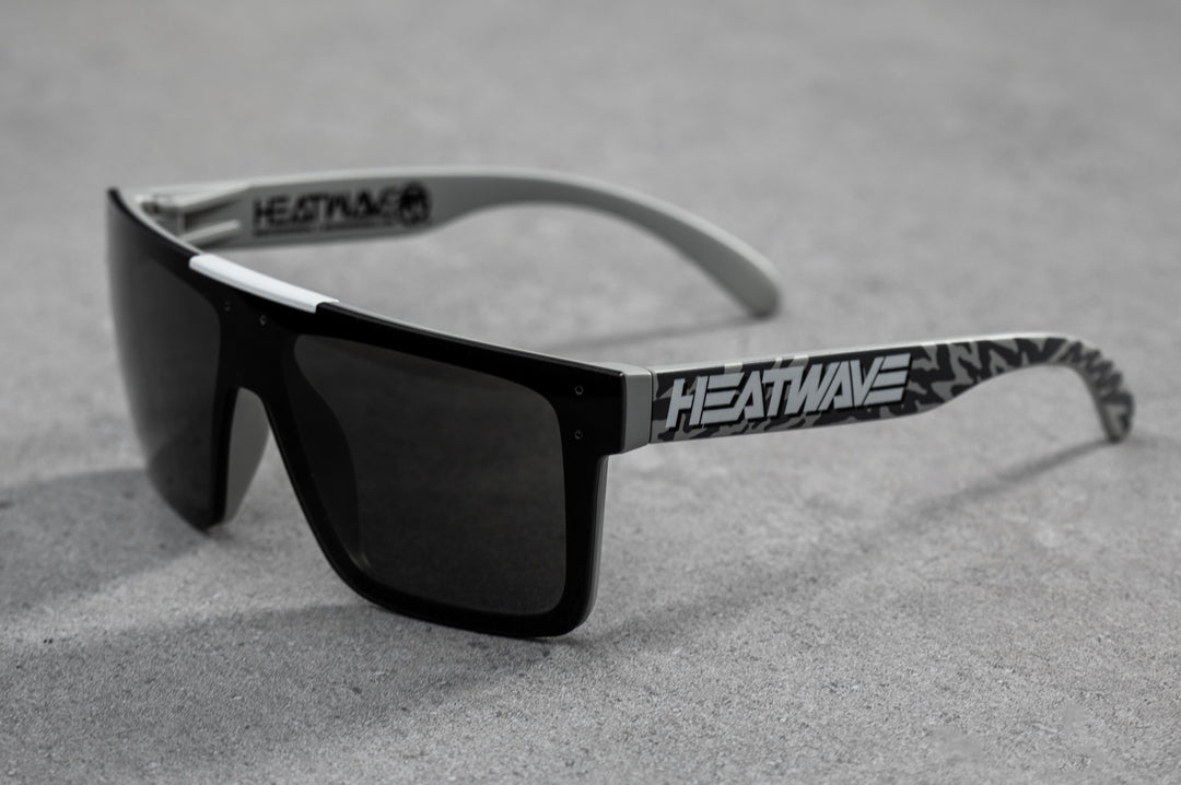 Side view of Heat Wave Visual Quatro Sunglasses with light grey frame, white logo print arms and black lens.