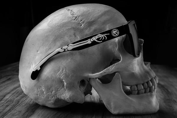 Photoshopped human skull wearing Heat Wave Visual Regulator Sunglasses with black frame, bones print arms and black lenses.