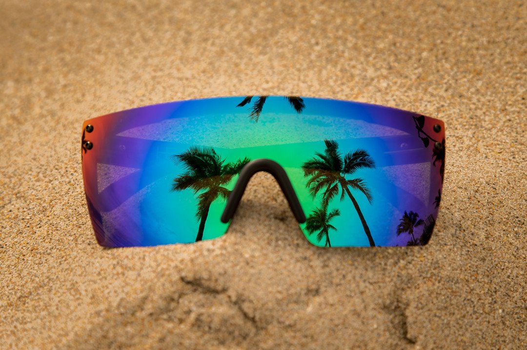 Heat Wave Visual Lazer Face Z87 Sunglasses with black frame and piff green lens lying on a sand beach looking at palm trees.