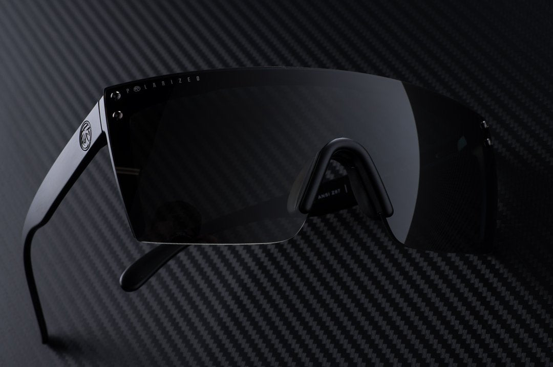 Heat Wave Visual Lazer Face Z87 Sunglasses with black frame and black lens lying sideways on carbon fiber.