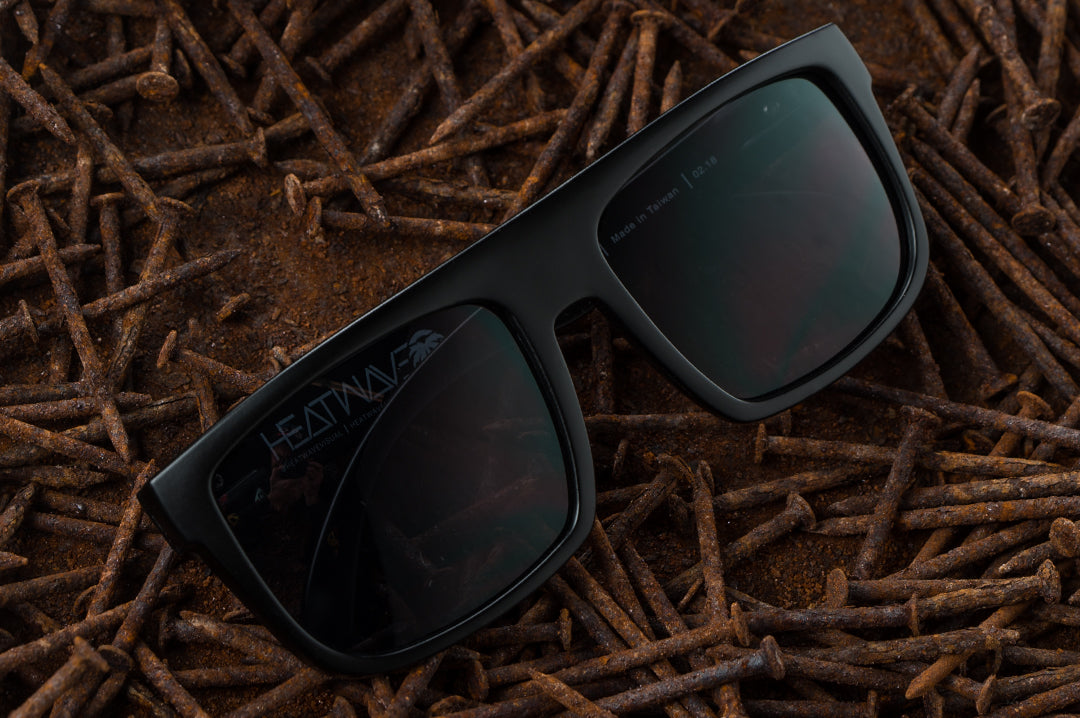 Front of Heat Wave Visual Z87 Regulator Sunglasses with black frame and black lenses laying in a bed of rusty nails.