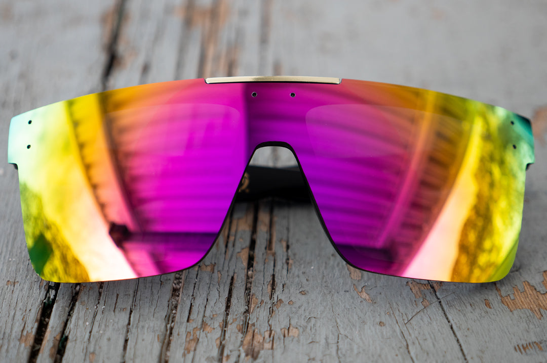 Heat Wave Visual Quatro Sunglasses with black frame and spectrum pink yellow lens laying on a wooden table.