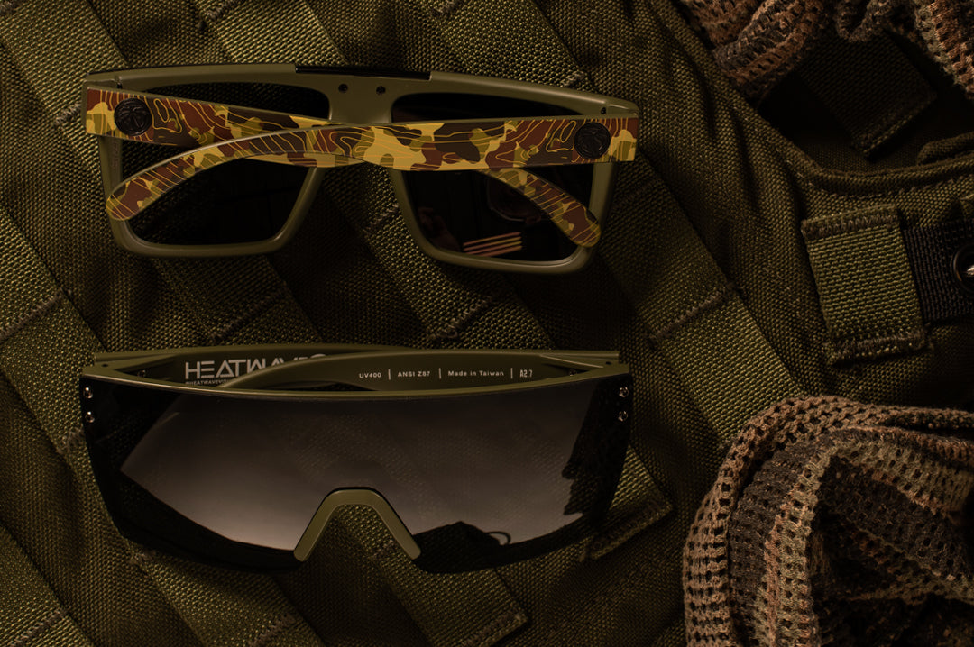 Two Heat Wave Visual Topo Camo Sunglasses lying on a military vest.