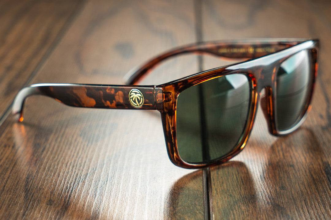 Heat Wave Visual Regulator Sunglasses with tortoise brown frame and black lenses sitting on wood floor.