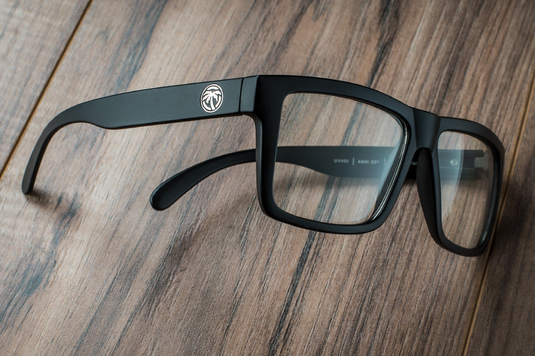 Side view of Heat Wave Visual Vise Z87 Sunglasses with black frame and clear lenses on a wooden table.