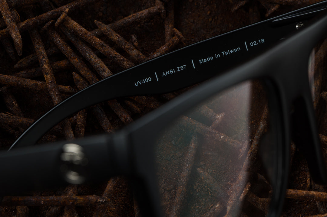 Inside view of Heat Wave Visual Z87 Regulator Sunglasses with black frame and polarized black lenses laying in a bed of rusty nails.